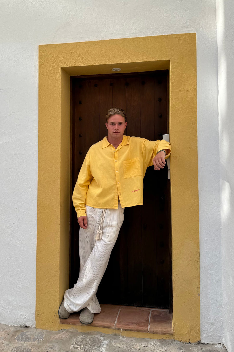 Modelo con camisa amarilla All day long y pantalón crudo All day pants Tela Bali en un portal de Ibiza