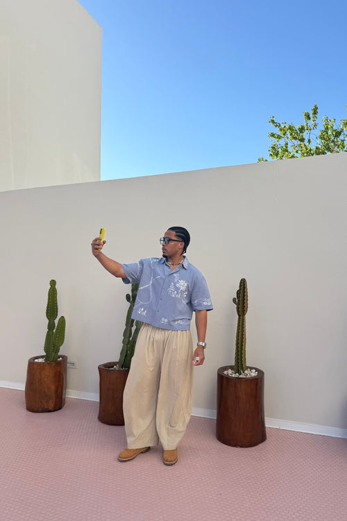 Modelo en una terraza con suelo rosa y cactus, con la camisa MDT way azul de bordados blancos y los Freedom pants blancos