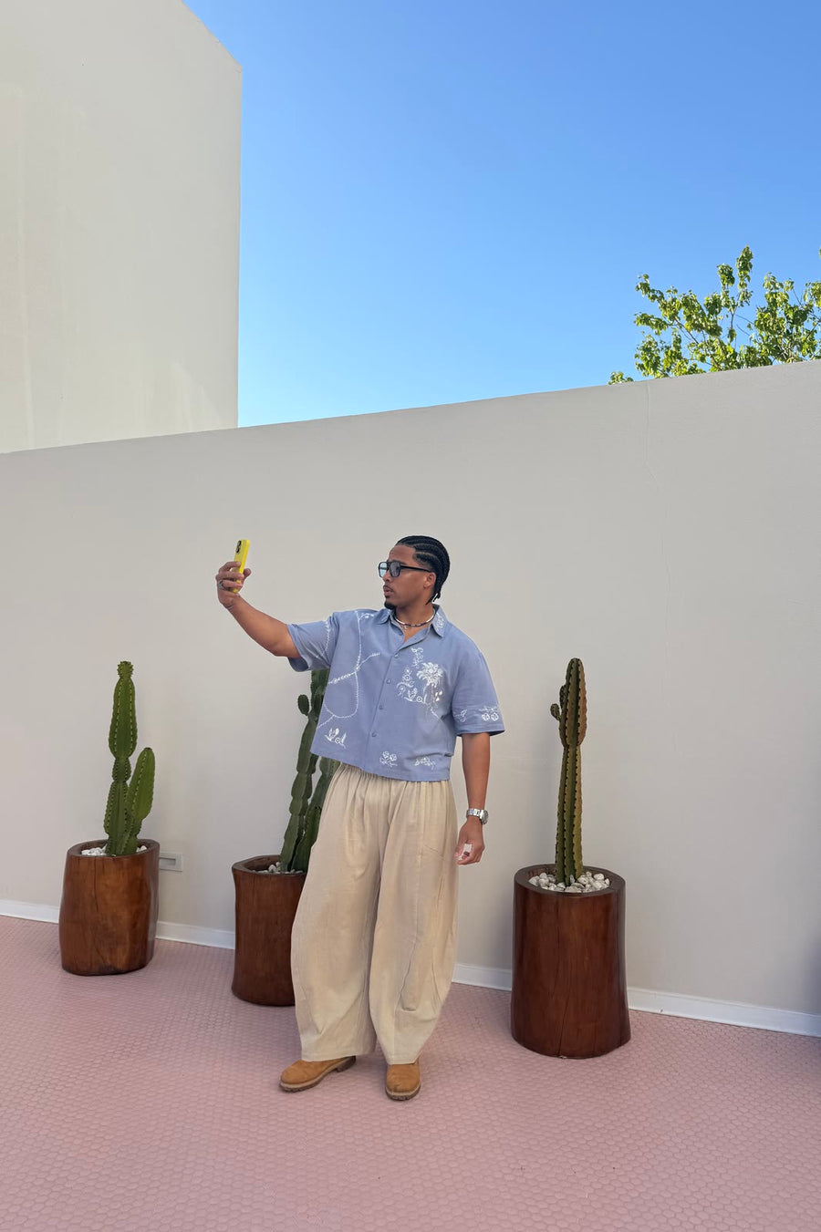 Modelo en una terraza con suelo rosa y cactus, con la camisa MDT way azul de bordados blancos y los Freedom pants blancos